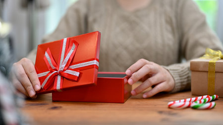 A woman open a beautiful Christmas gift box at her table. Christmas or New year holiday concept....