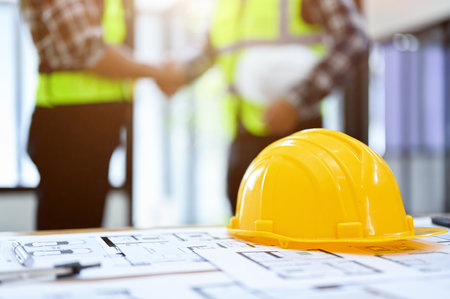 Engineer or construction worker workspace with a yellow hardhat and blue print on a table against a...