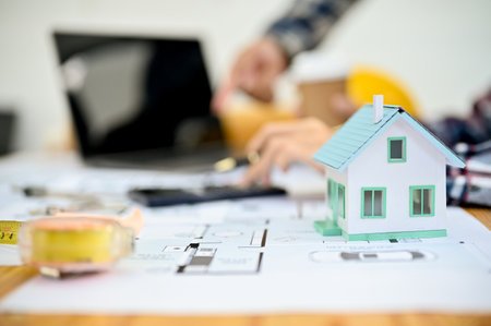 Engineer or architect desk workspace with house model, measuring tape, blueprint and calculator....