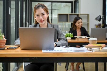 Charming Asian young businesswoman or female office worker working on her project on laptop computer in co-working office space.の写真素材