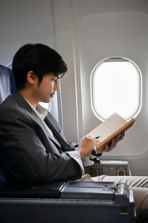 Portrait, A professional young Asian businessman is on the flight, reading, checking or writing...