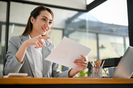 Attractive young Asian businesswoman holding a paper or document, working at her office desk.の写真素材
