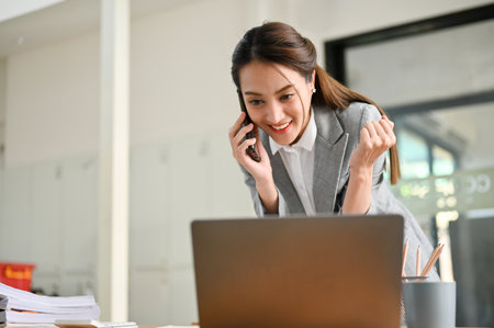 Attractive and charming young Asian female account executive or marketing assistant dealing business through the phone with her partner, making a good deals on the phone call.の写真素材