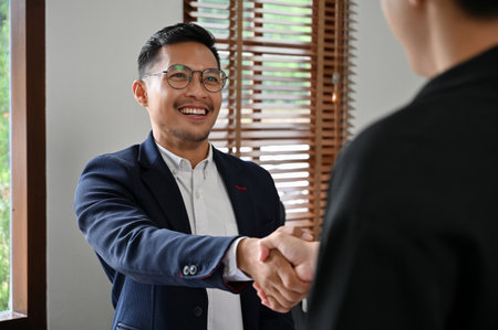 Smart and successful millennial Asian businessman or male executive manager shaking hand with his business partner in the meeting.の写真素材