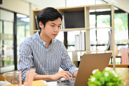 Handsome and smart young Asian male freelancer or businessman remote working in the coffee shop, using laptop computer to manage his work.の写真素材