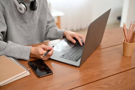 A hipster young Asian male freelancer working on his project on laptop computer at home. cropped shot, work from home conceptの写真素材