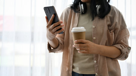 A hipster young Asian girl using her smartphone and holding a coffee cup. cropped shot
