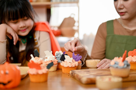 selective focus, Delicious and yummy Halloween cupcakes on dining table. Mom and cute daughter making Halloween cupcakes together.の写真素材