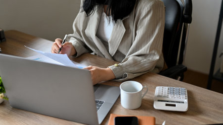 An Asian businesswoman or female accountant reviewing sales report, working at her office desk. cropped imageの写真素材