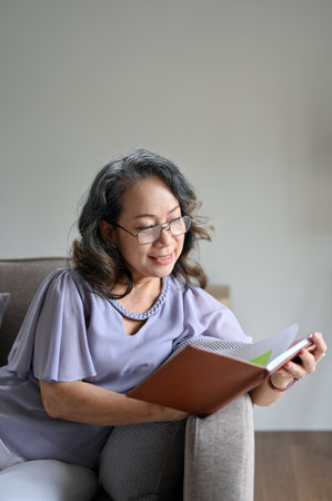 Portrait, Attractive Asian aged woman wearing eyeglasses relaxing on her comfortable sofa in her...