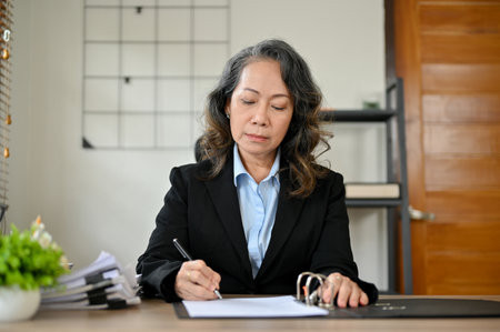 Professional Asian-aged businesswoman or female senior account manager in a formal suit, sign her signature on a document.の写真素材