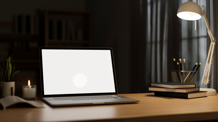 close-up image, Modern office desk workspace under the warm light from table lamp in the darkness room with laptop white screen mockup and accessories. 3d rendering, 3d illustrationの写真素材