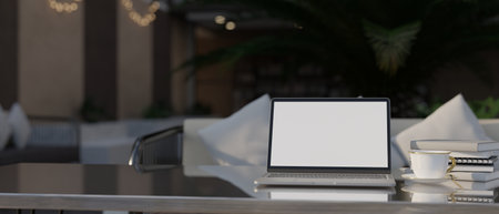 Laptop white screen mockup, coffee cup, books and copy space on stylish tabletop over blurred restaurant or coffee shop seating space in the background. 3d render, 3d illustrationの写真素材