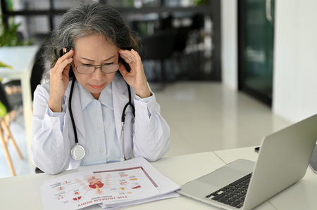 Stressed and professional Asian aged female doctor concentrating on her medical research case and...