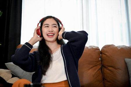 Beautiful and happy young Asian female sings a song while listening to music on her headphones in the living room.の写真素材