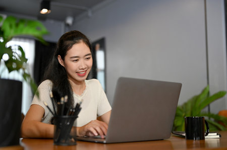 Pretty and charming young Asian female office worker or college student in the coffee shop, using her laptop computer. remote working and workplace conceptの写真素材