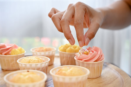 Close up view of woman decorating her fresh baked homemade cupcake in the kitchenの写真素材