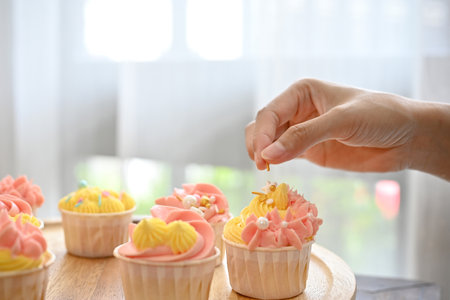 Cropped shot of cupcake with woman hand decorating the cupcake in the kitchen