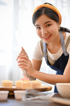 Beautiful woman making cupcake, decorating cupcake with cream in the kitchenの写真素材
