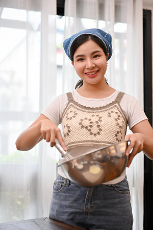 Portrait, Beautiful attractive young Asian female holding a mixing bowl, baking a homemade cupcake in the kitchen.の写真素材