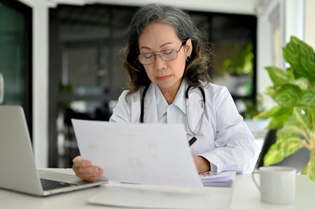 Professional Asian aged female doctor concentrating on her medical research, working at her desk in the doctor's office.の写真素材