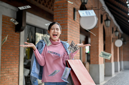 Overjoyed and carefree young Asian female shopper screaming with joyful feelings, carrying her shopping bags, and throwing up money. rich, wealth, shopaholicの写真素材