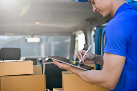 Close up view of delivery man in blue uniform checking package on tablet before sending to the...