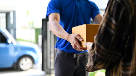 Close up view of delivery man in blue uniforms handing the parcel  to customer while standing in...