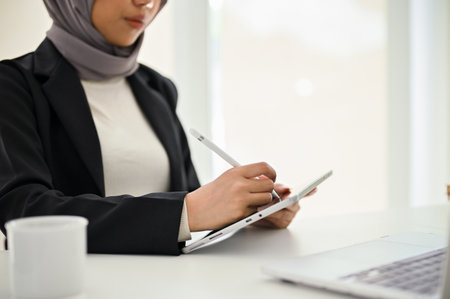 Close-up shot of a professional and beautiful Muslim businesswoman using digital tablet at her office desk.の写真素材