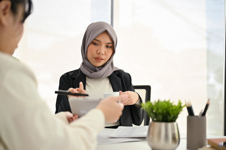 Professional Asian Muslim female boss in the meeting with her team, consulting and discussing plan for new project.の写真素材