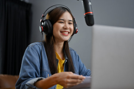 Cheerful and happy young Asian female podcaster or freelance online radio host in her studio, laughing and enjoys talking with her guest from the call. Podcast contentの写真素材