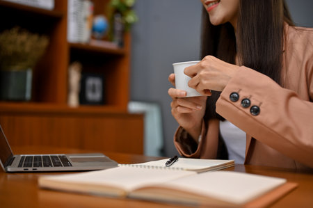 cropped image, Beautiful Asian businesswoman or office worker at her office desk, looking an information on laptop screen while sipping morning coffee.の写真素材