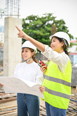 Beautiful and professional young Asian female engineer and female architect are discussing and planning the building plan at the construction site together.の写真素材