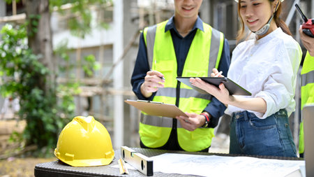 Beautiful attractive Asian female architect checking some details on clipboard during meeting with a...