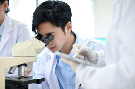 Talented young Asian male scientist looking under the Microscope, working with his colleagues in the...