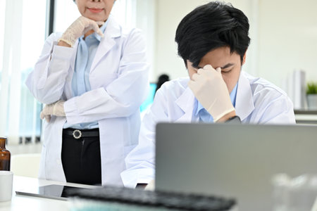 Unhappy and stressed young Asian male scientist sits at his office desk in the laboratory after getting a complaint from his female supervisor.の写真素材