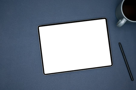 Top view, Workspace with portable tablet white screen mockup, coffee cup and pen on blue background.の写真素材