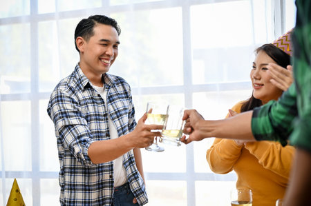 Happy Asian man toasting and clinking his glass of wine with friends in the party, celebrating their special moment together.の写真素材