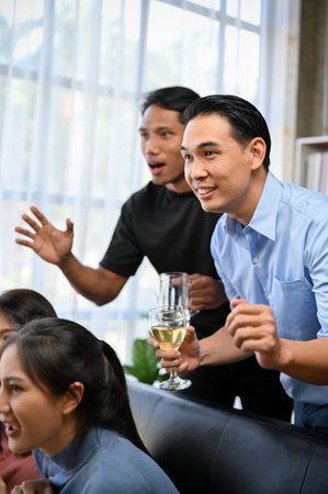 Two excited Asian male friends football fans watching football or soccer in a national match on TV at home together. sports and entertainment conceptの写真素材
