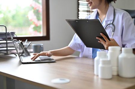 cropped image, Professional young Asian female doctor concentrating on her medical research, using laptop, working in the doctor's office.の写真素材