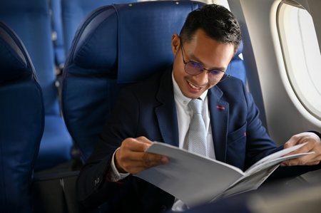 Happy and successful Asian businessman is in business class reading a magazine during the flight to an overseas business meeting.の写真素材