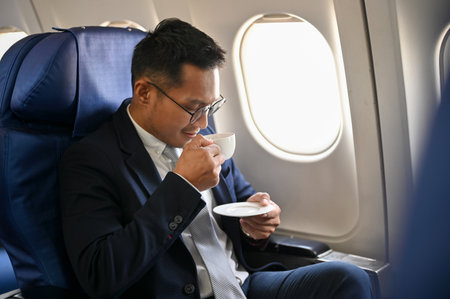 Successful Asian businessman or male CEO sits at the window seat on his private jet sipping coffee during the flight for an overseas business meeting.の写真素材