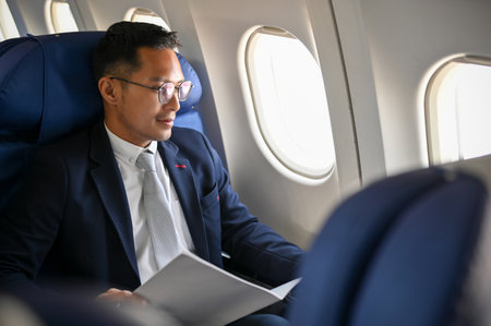 Successful Asian businessman or male CEO in a formal business suit sits at the window in business class, traveling for an overseas business meeting.の写真素材
