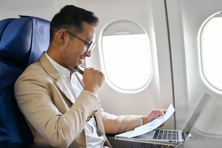Smart and professional Asian businessman reading contract, using laptop and working during the flight. side view imageの写真素材