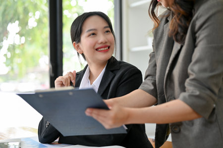 Charming and happy young Asian female office worker is being trained by her boss, getting project compliments from her boss.の写真素材