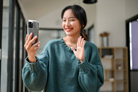 Happy and charming young Asian woman enjoys talking on video call through her phone with her family.の写真素材