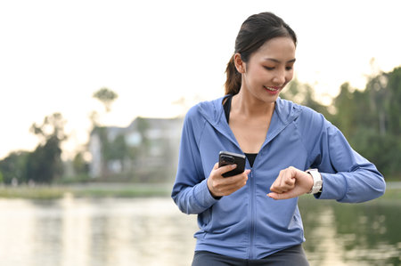 Happy and sporty fit Asian woman in sportswear holding her phone and checking her heart rate and...