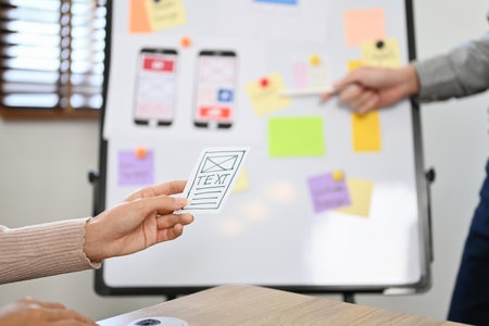 A female hand holding a mobile application interface design paper over the blurred background of the...