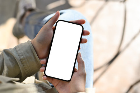 Close-up image, A female's hands holding a smartphone white screen mockup over blurred background.の写真素材