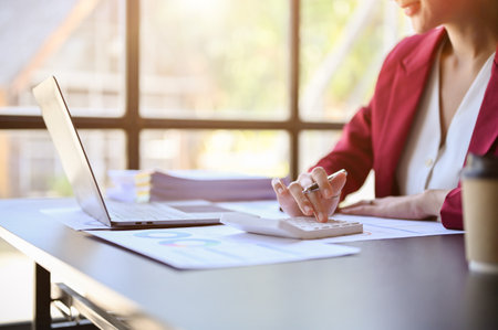 Professional businesswoman or female financial analyst working on financial report, using calculator, analyzing financial data at her desk. cropped imageの写真素材